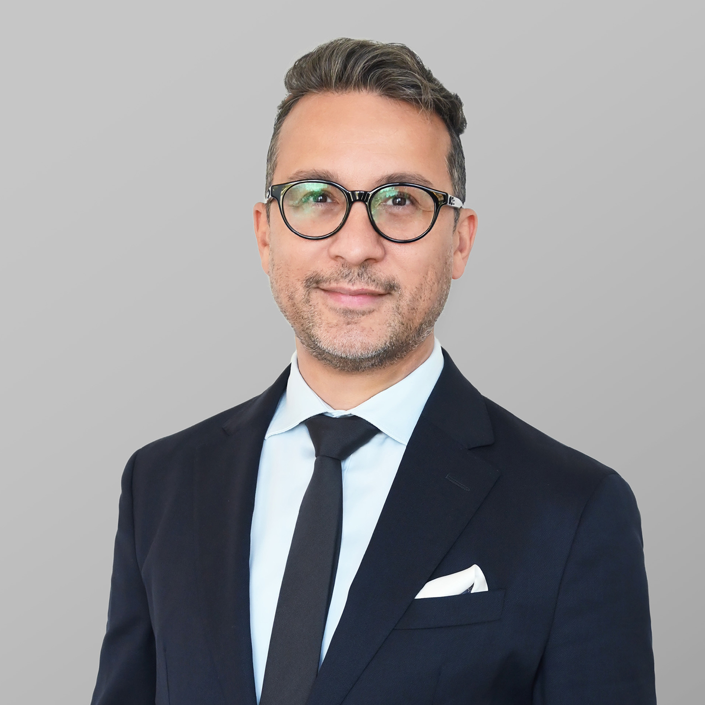 Business professional in a navy suit with arms crossed standing against a light gray background.