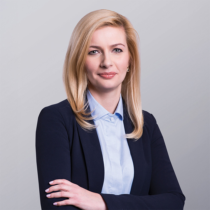 Business professional in a navy suit with arms crossed standing against a light gray background.