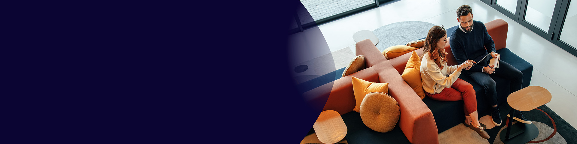 Colleagues discussing insights on a tablet while seated on colorful lounge chairs in an open workspace.