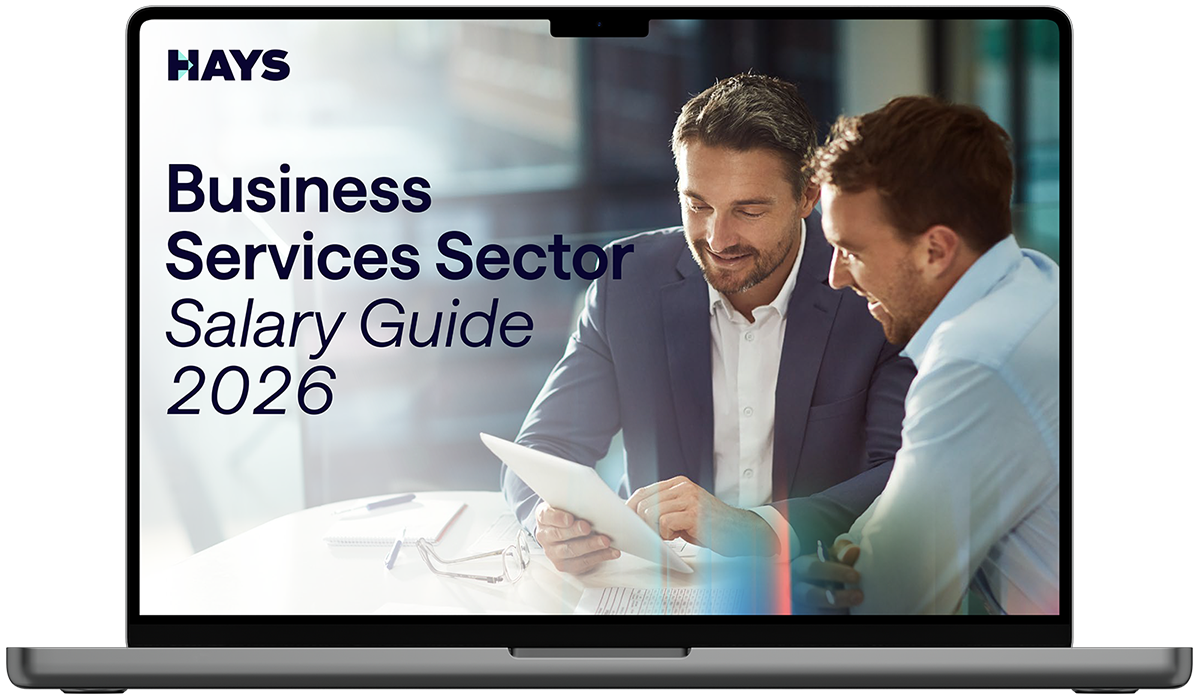 Laptop screen displaying the Hays Belgium Salary Guide 2026 cover, featuring text on a blue background with a person in business attire in the foreground and others in the background.